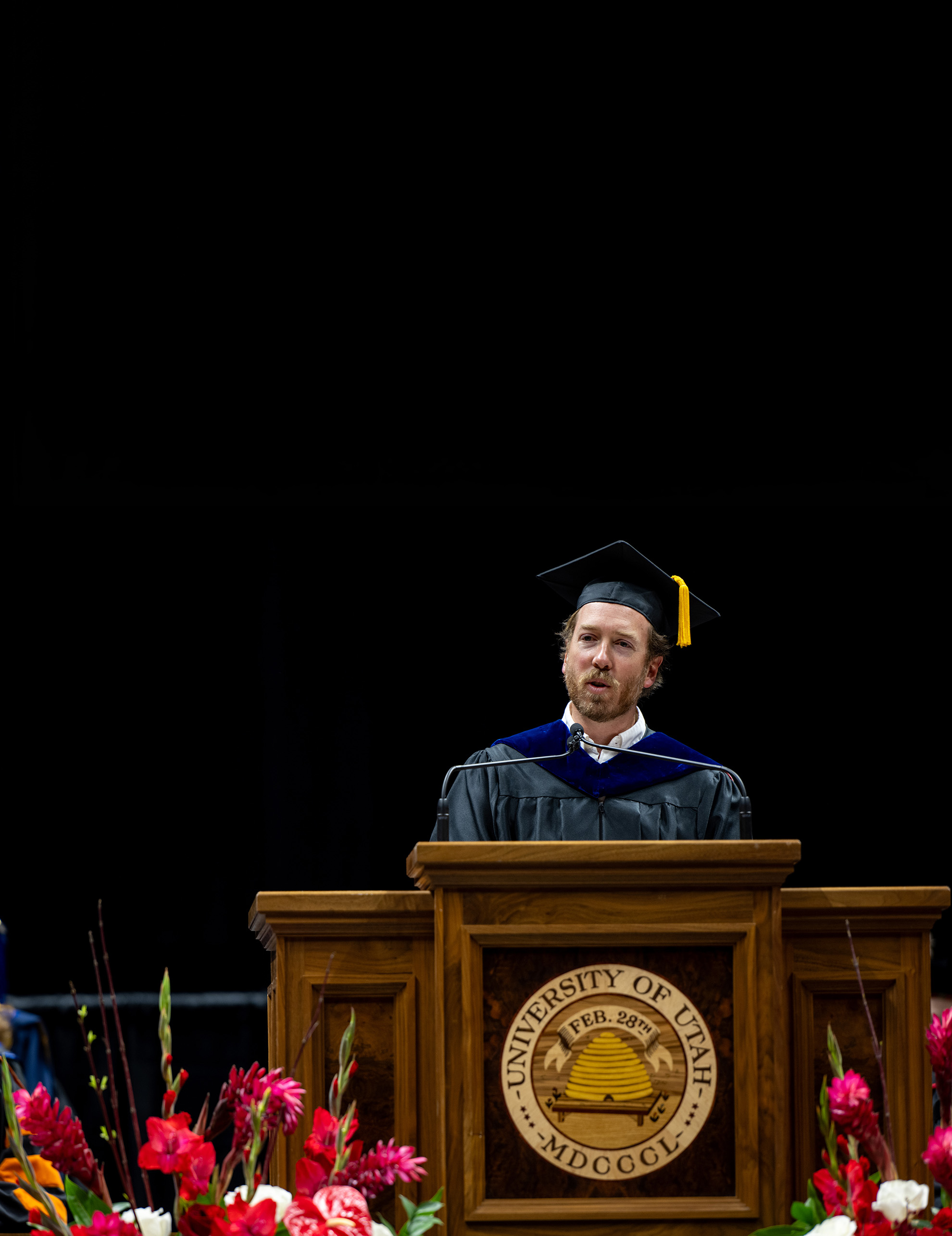 Kevin Knight in graduation regalia at the podium giving his speech